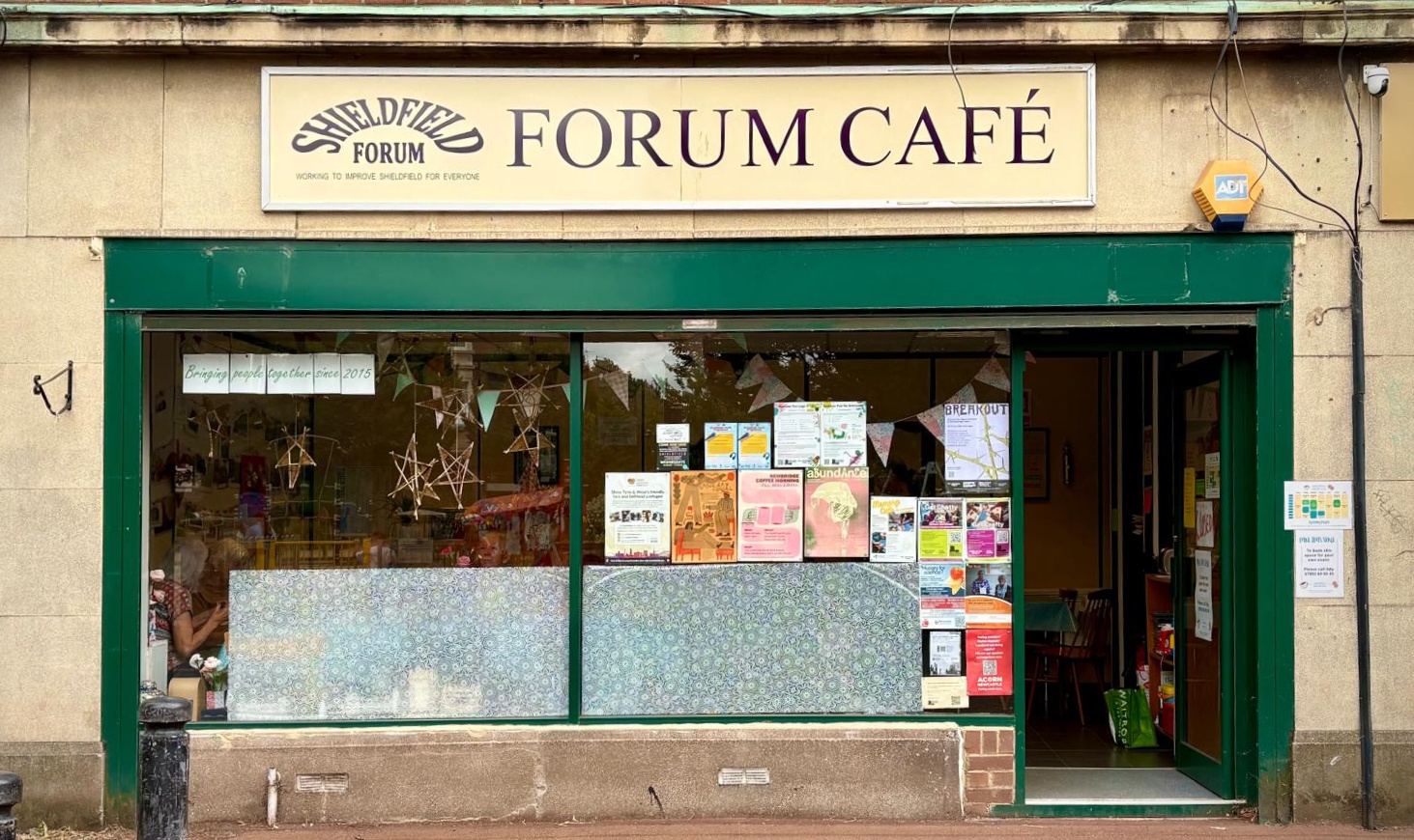 The Forum Café shopfront in Shieldfield — a cream signboard reading Forum Café above a deep-green painted frontage.